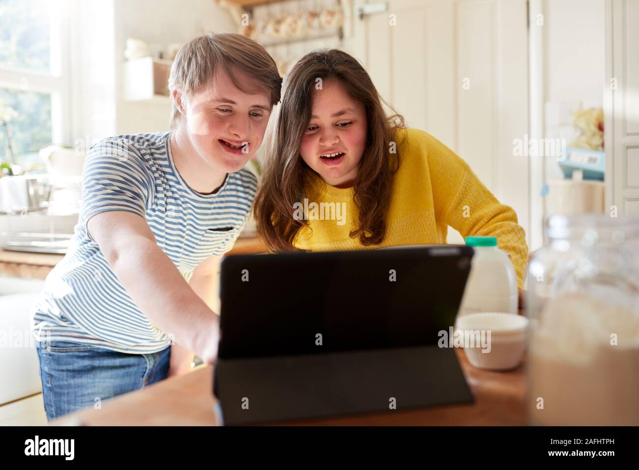 Jeune couple Trisomie recette suivante sur tablette numérique pour faire cuire des gâteaux dans la cuisine à la maison Banque D'Images