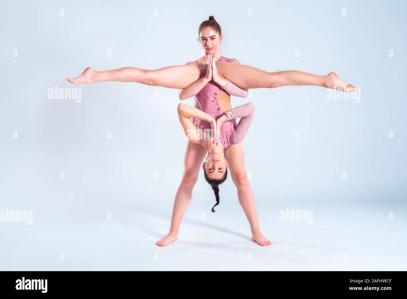 Deux gymnastes filles flexibles avec des nattes, en rose justaucorps sont l'exécution par le biais d'appuyer tout en se posant isolé sur fond blanc. Close-up. Banque D'Images