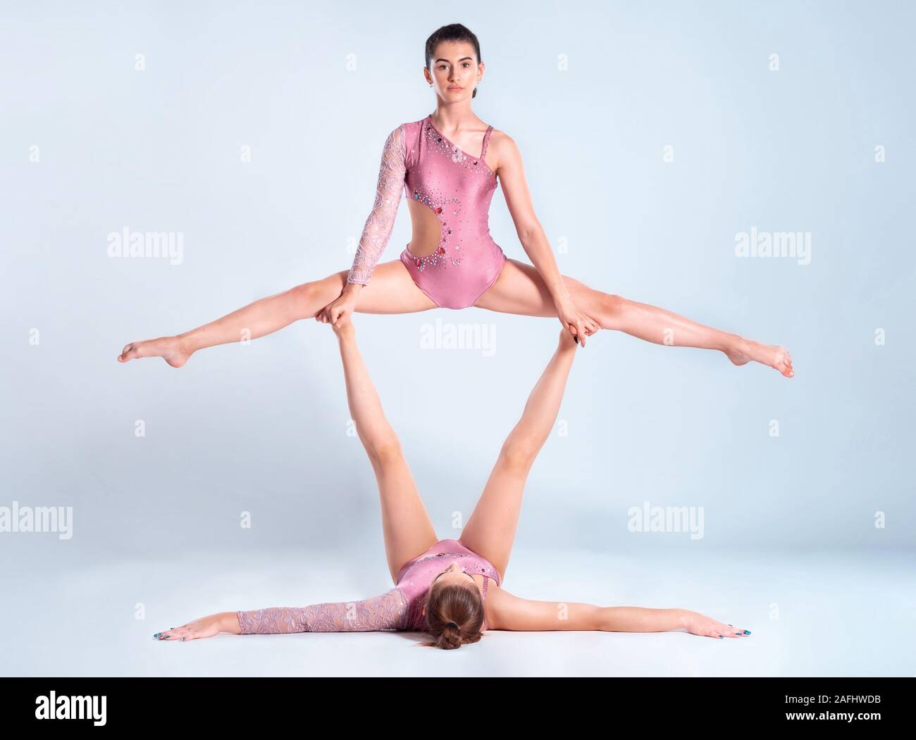 Deux gymnastes filles flexibles avec des nattes, en rose justaucorps sont l'exécution par le biais d'appuyer tout en se posant isolé sur fond blanc. Close-up. Banque D'Images