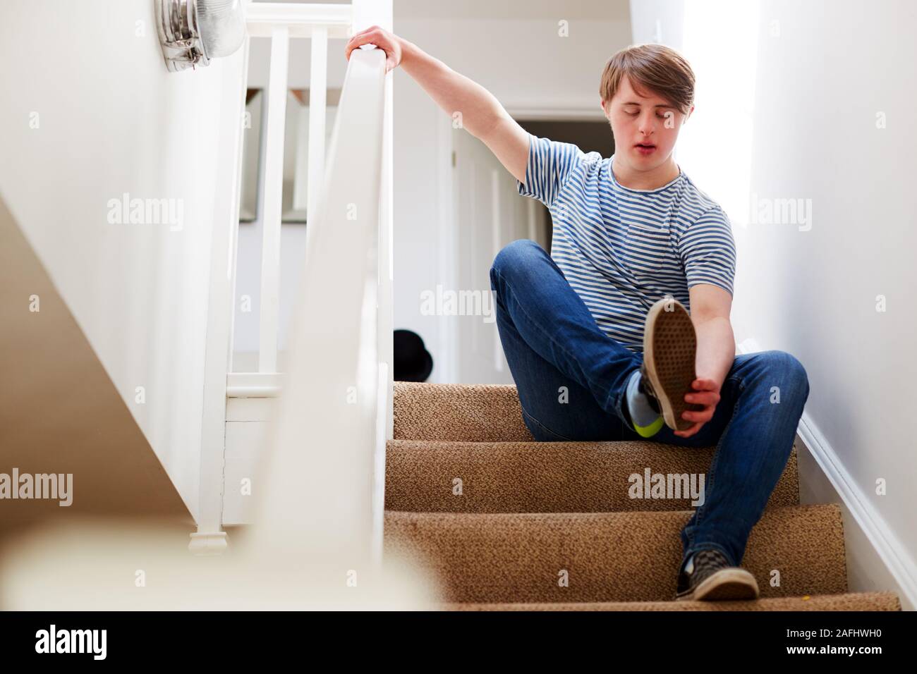 Jeune homme assis sur le syndrome de Down Stairs mise sur des chaussures à domicile Banque D'Images