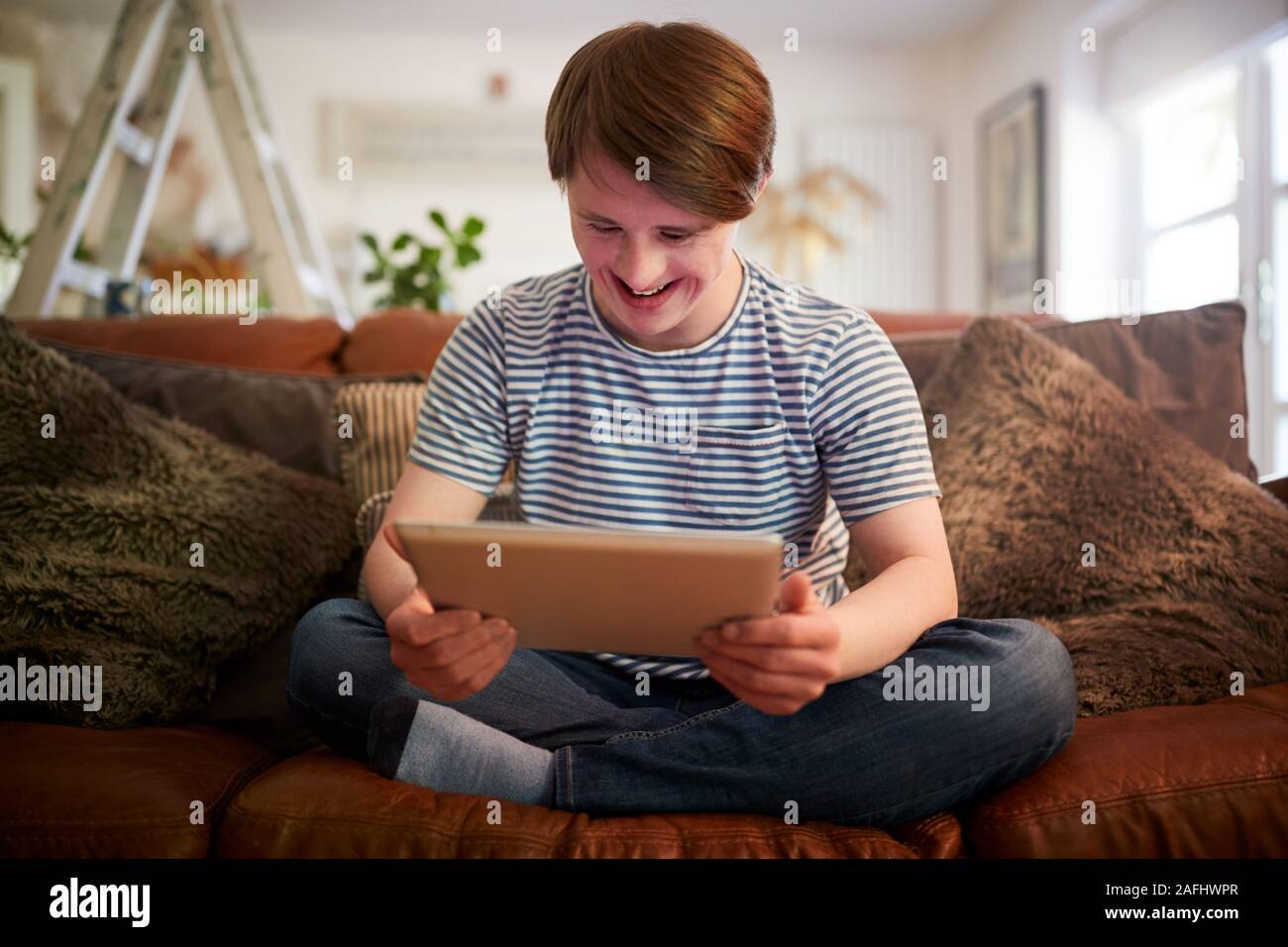 Le syndrome de Down Young Man Sitting on Sofa Using Digital Tablet Banque D'Images