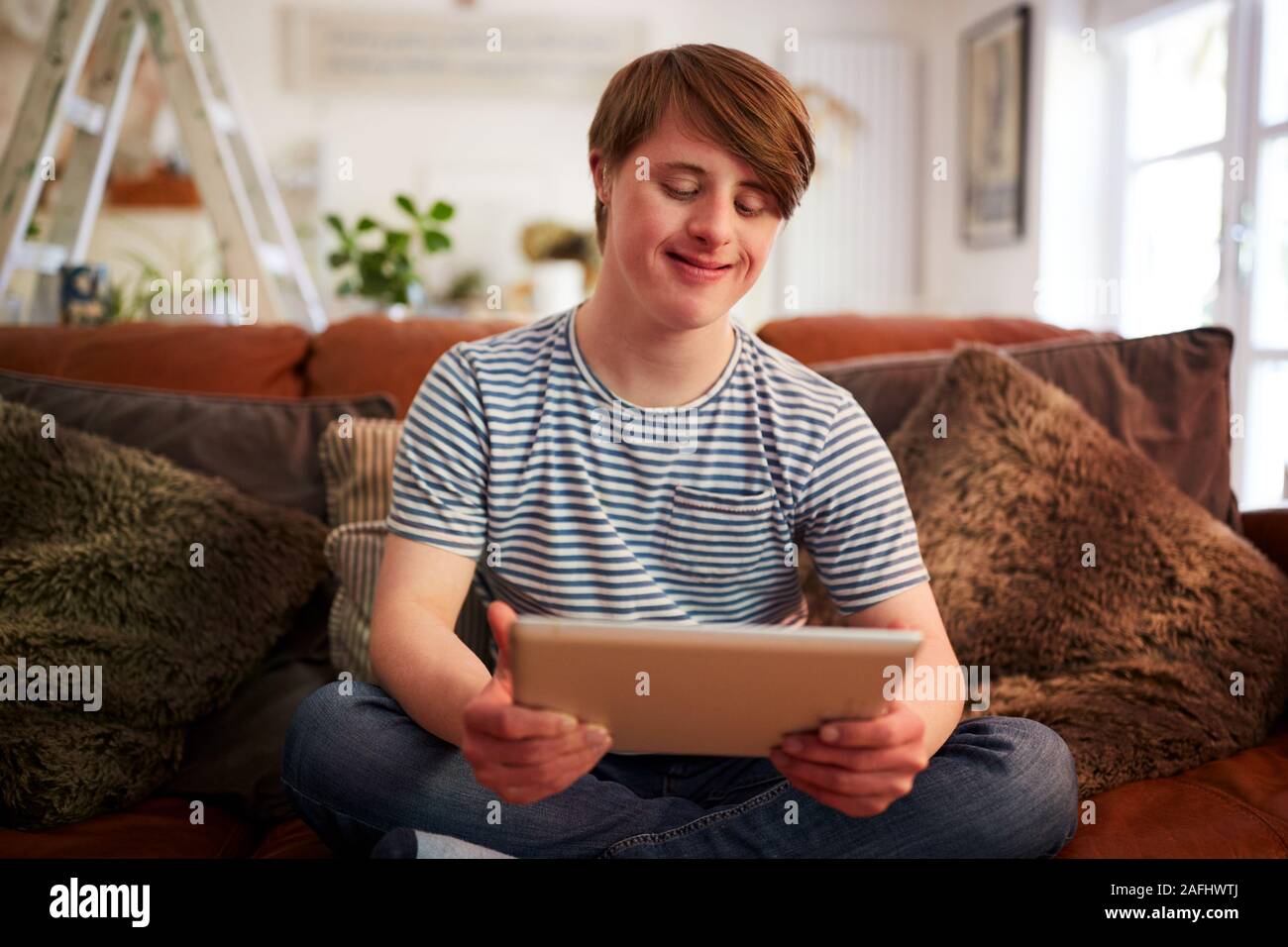 Le syndrome de Down Young Man Sitting on Sofa Using Digital Tablet Banque D'Images
