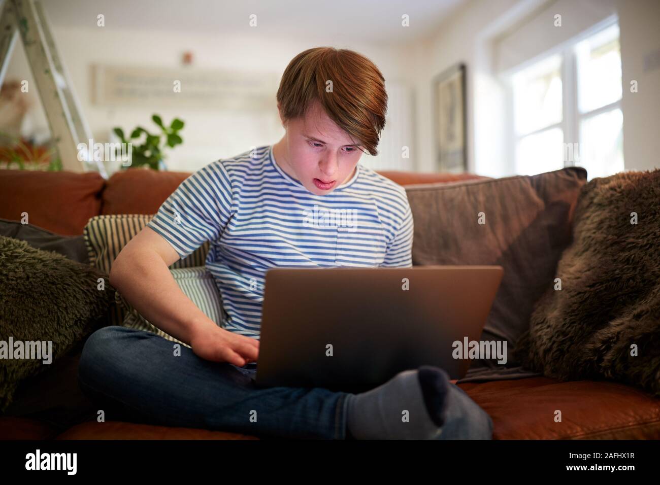 Le syndrome de Down Young Man Sitting on Sofa Using Laptop At Home Banque D'Images