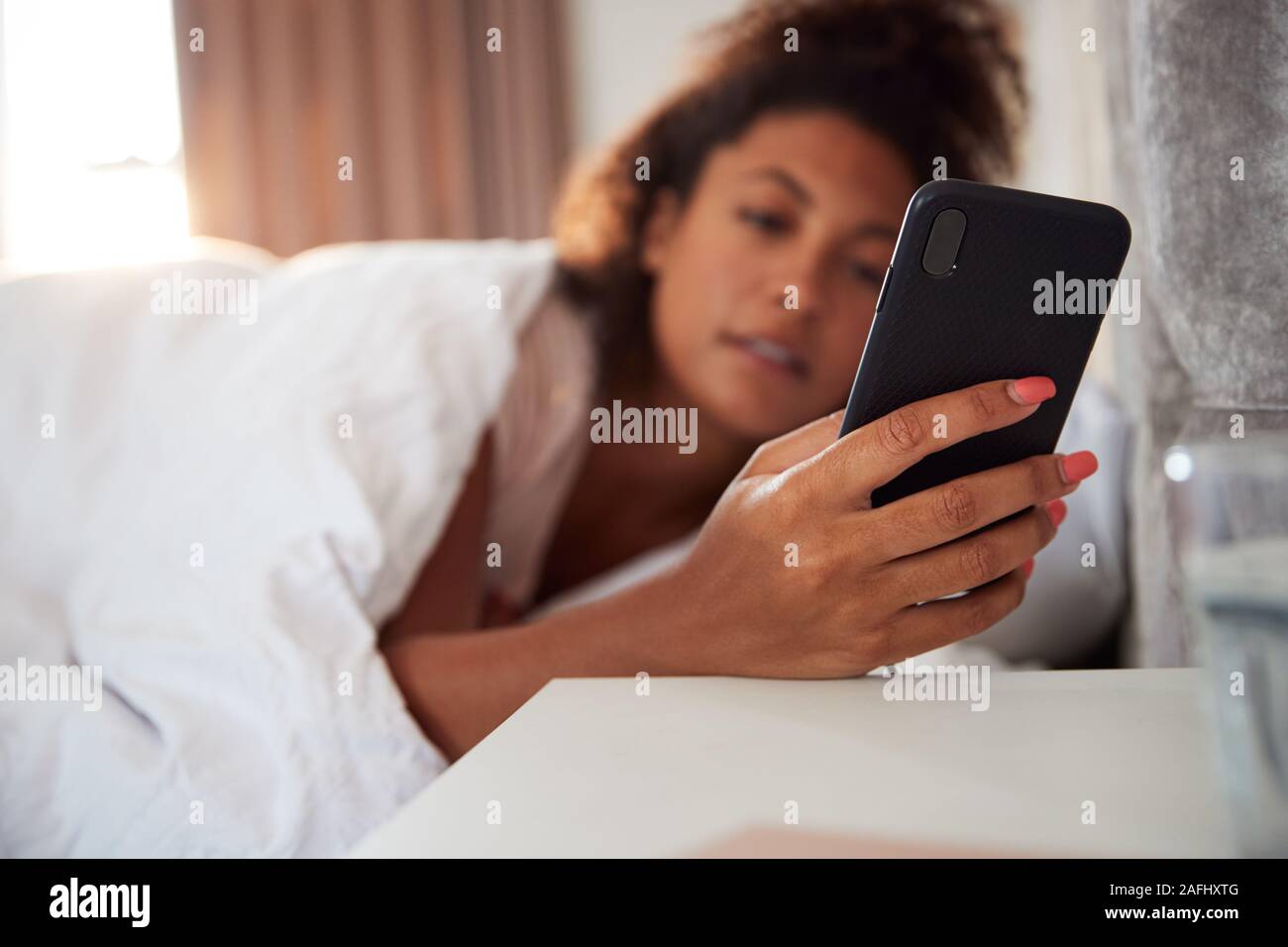 Woman Waking Up In Bed immédiatement tend la main à regarder le téléphone mobile Banque D'Images