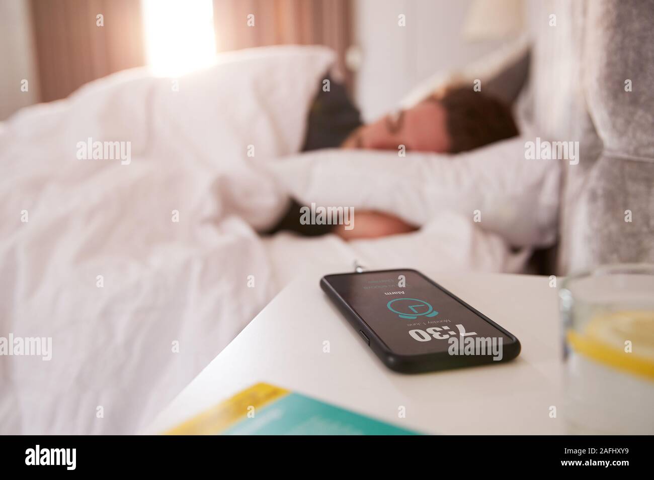 Homme endormi au lit avec table de chevet sur téléphone mobile Banque D'Images