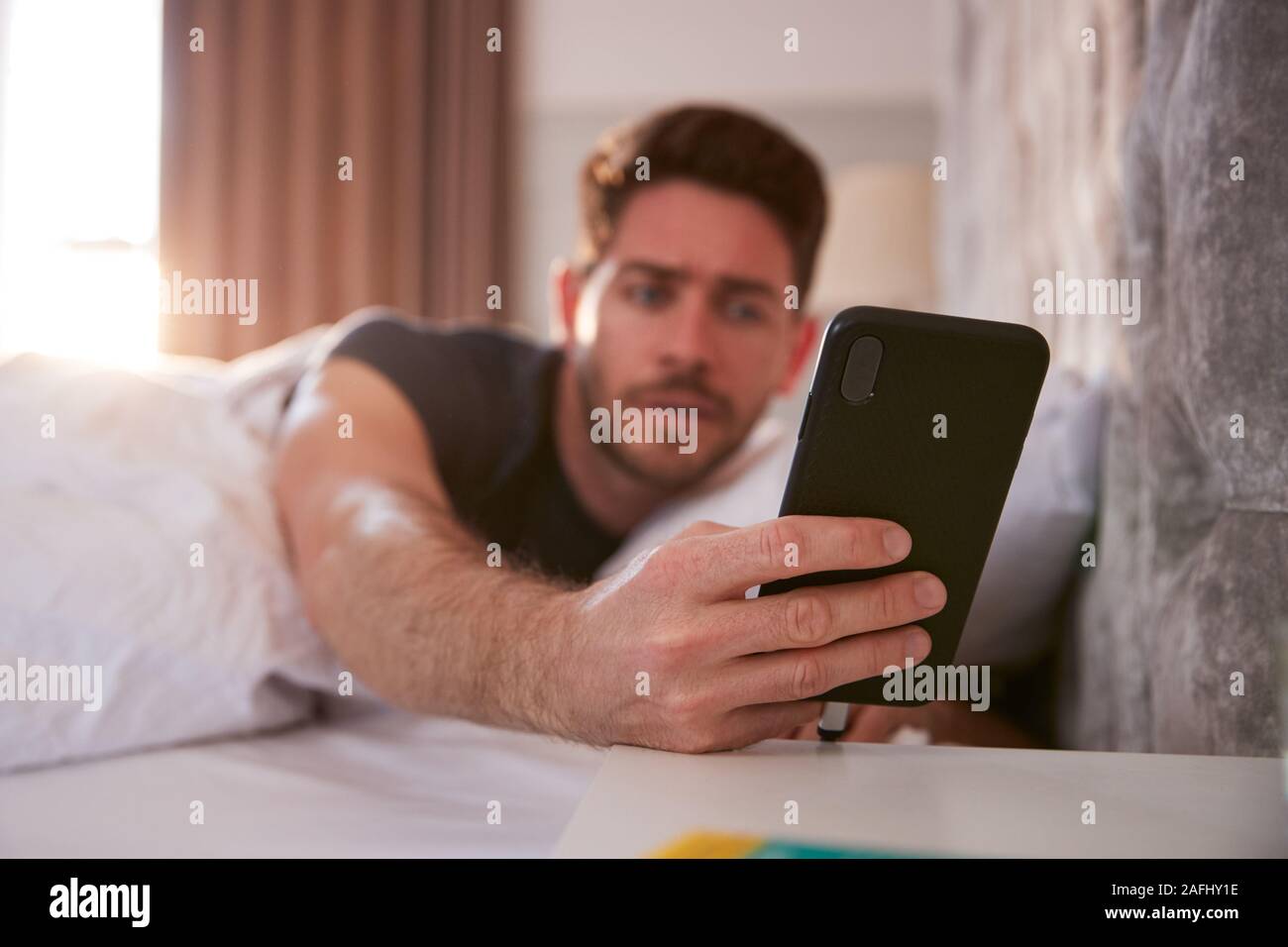 L'homme se réveiller dans le lit immédiatement tend la main à regarder le téléphone mobile Banque D'Images