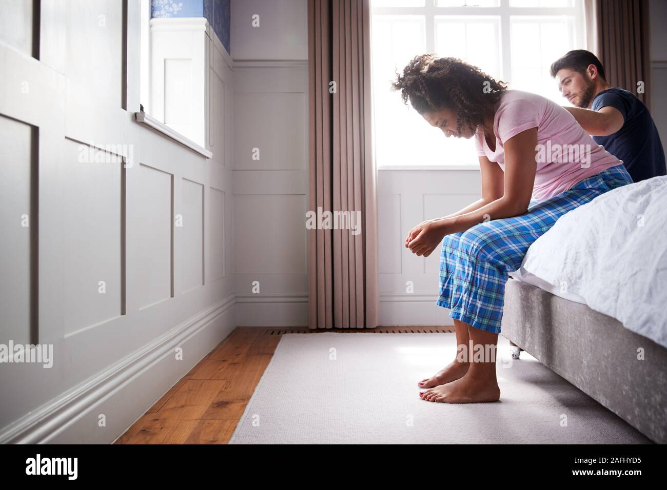 Homme Femme réconfortante Wearing Pajamas souffrant de dépression assis sur le lit à la maison Banque D'Images