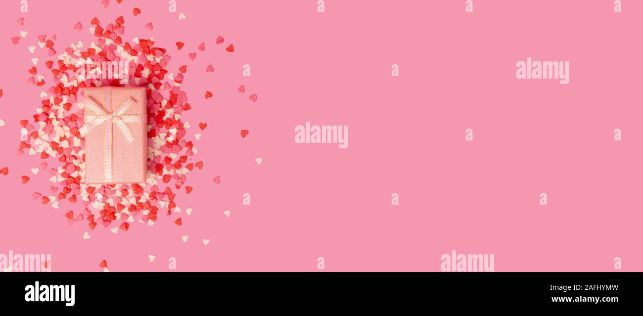 Boîte cadeau rose avec un arc dans le centre de l'image sur fond de bonbons coeur doux peu dispersées sur un fond rose. Vue de dessus. Banque D'Images
