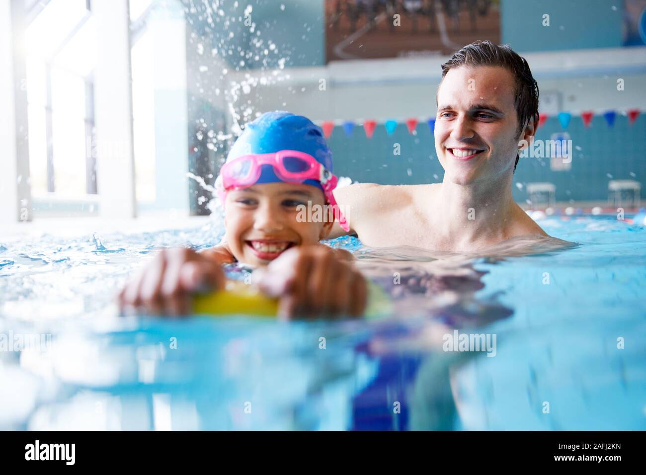 L'entraîneur de natation masculine Girl Holding donnant un flottement d'une leçon en piscine Banque D'Images