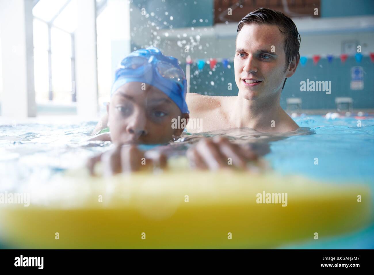 L'entraîneur de natation homme Boy Holding donnant un flottement d'une leçon en piscine Banque D'Images