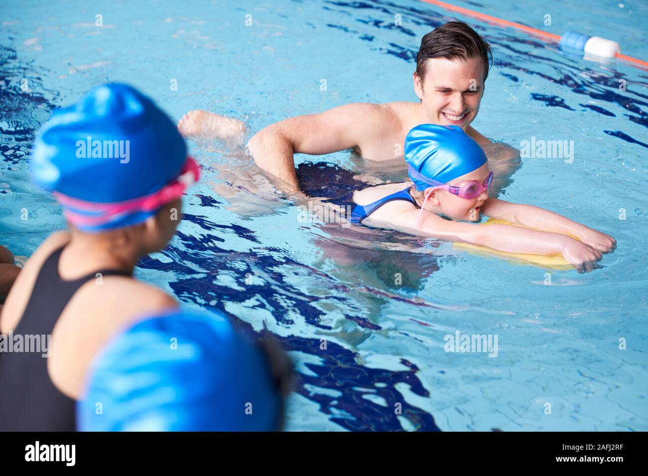 Entraîneur masculin dans l'eau donnant un groupe d'enfants leçon de natation en piscine couverte Banque D'Images