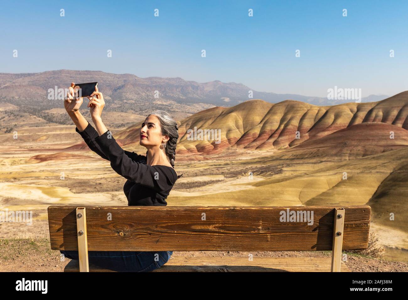 Une jeune brune avec des volets gris rend vos autoportraits assis sur un banc dans les collines peintes donnent sur Banque D'Images