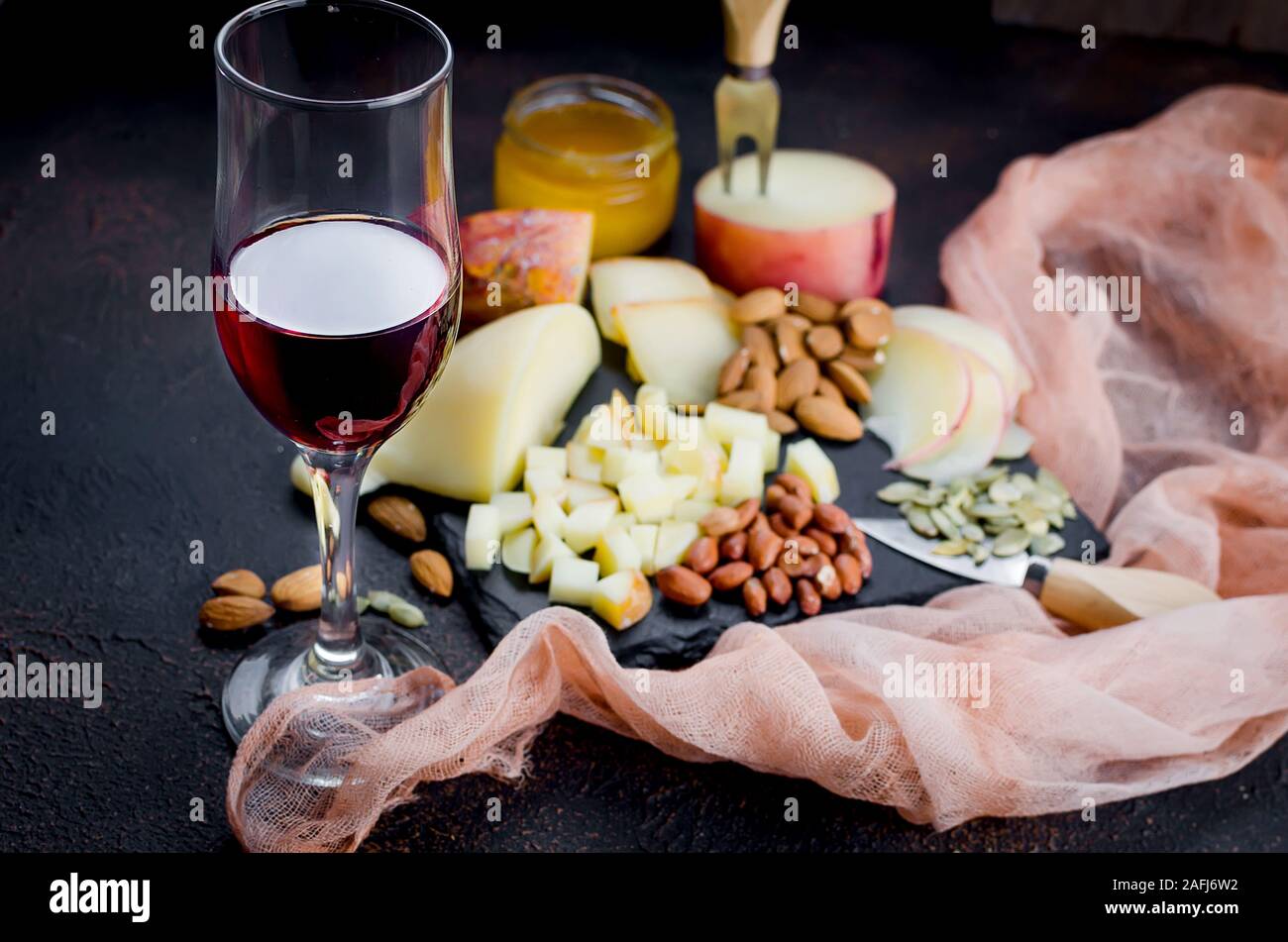 Verre de vin rouge, différentes variétés de fromage, d'amandes, miel en pot sur table en bois foncé Banque D'Images