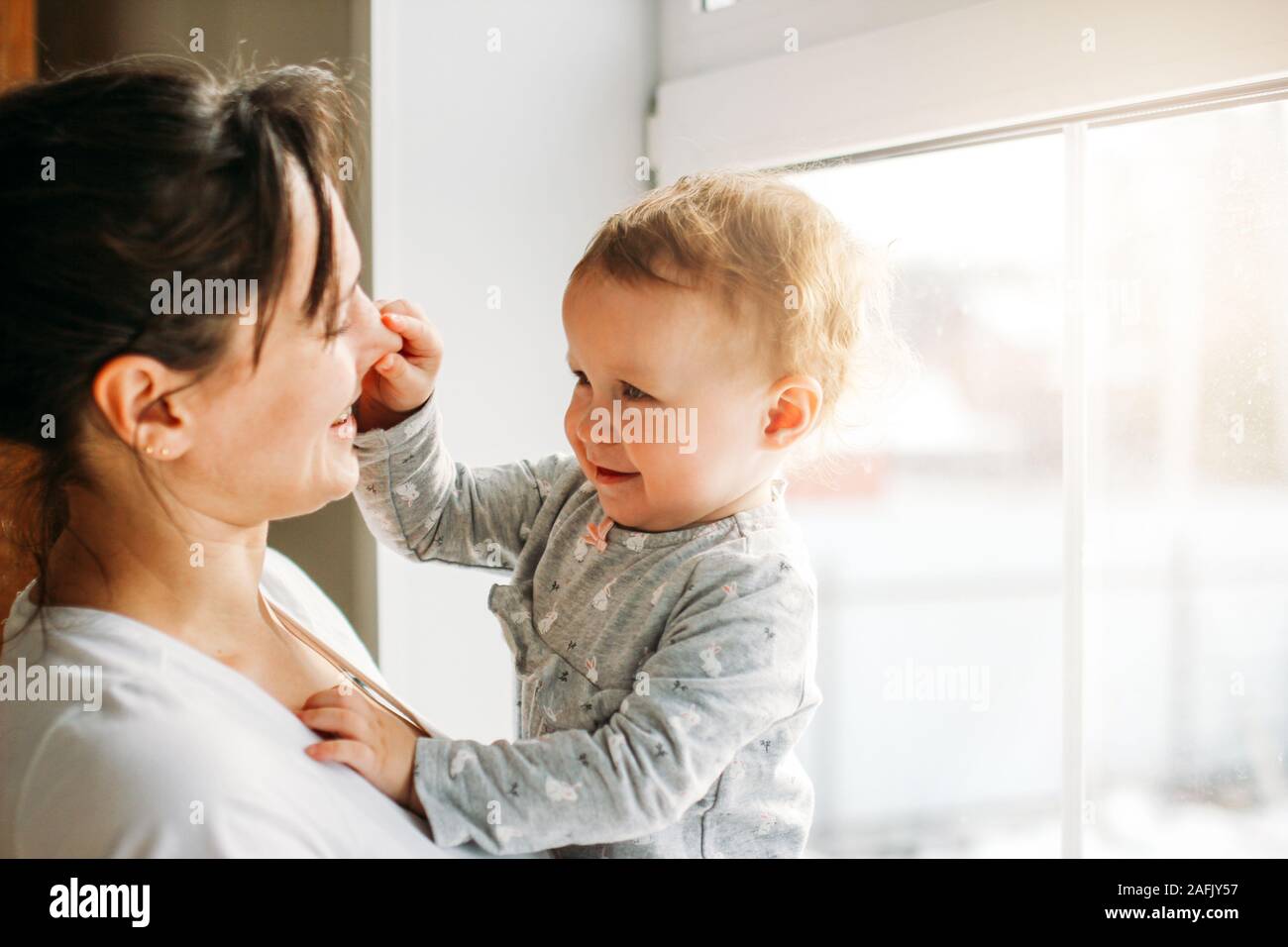 Jeune femme maman avec bébé fille sur mains près de fenêtre à l'accueil Banque D'Images
