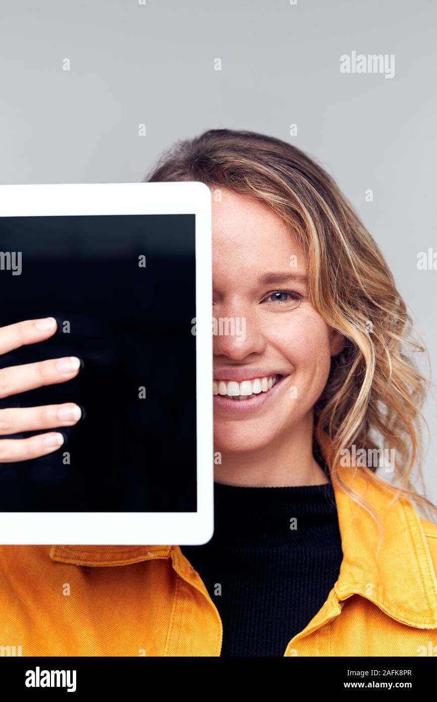 Studio Portrait Of Smiling Young Woman Covering Face With Digital Tablet Banque D'Images