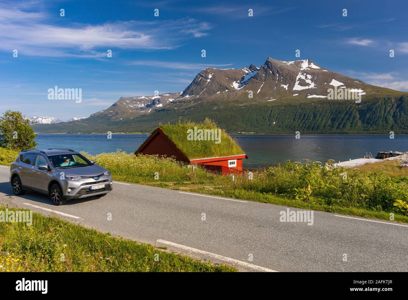 L'ÎLE DE KVALØYA, BAKKEJORD, NORVÈGE - automobile passe toit gazon immeuble sur l'île de Kvaløya en premier plan, et vue de l'Straumsfjorden fjord et montagnes. Banque D'Images