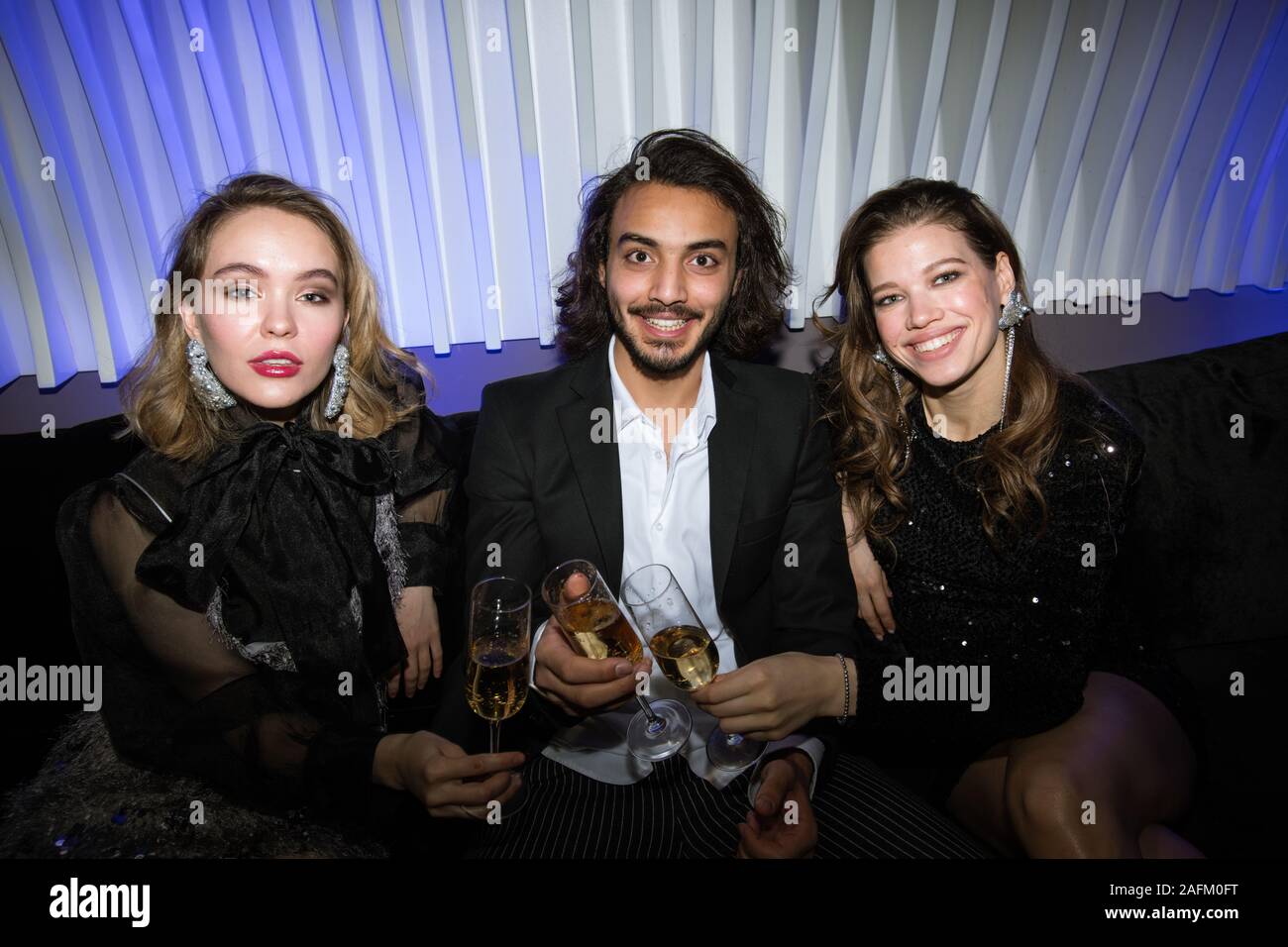 Trois jeunes amis glamour avec des flûtes de champagne sitting on couch Banque D'Images