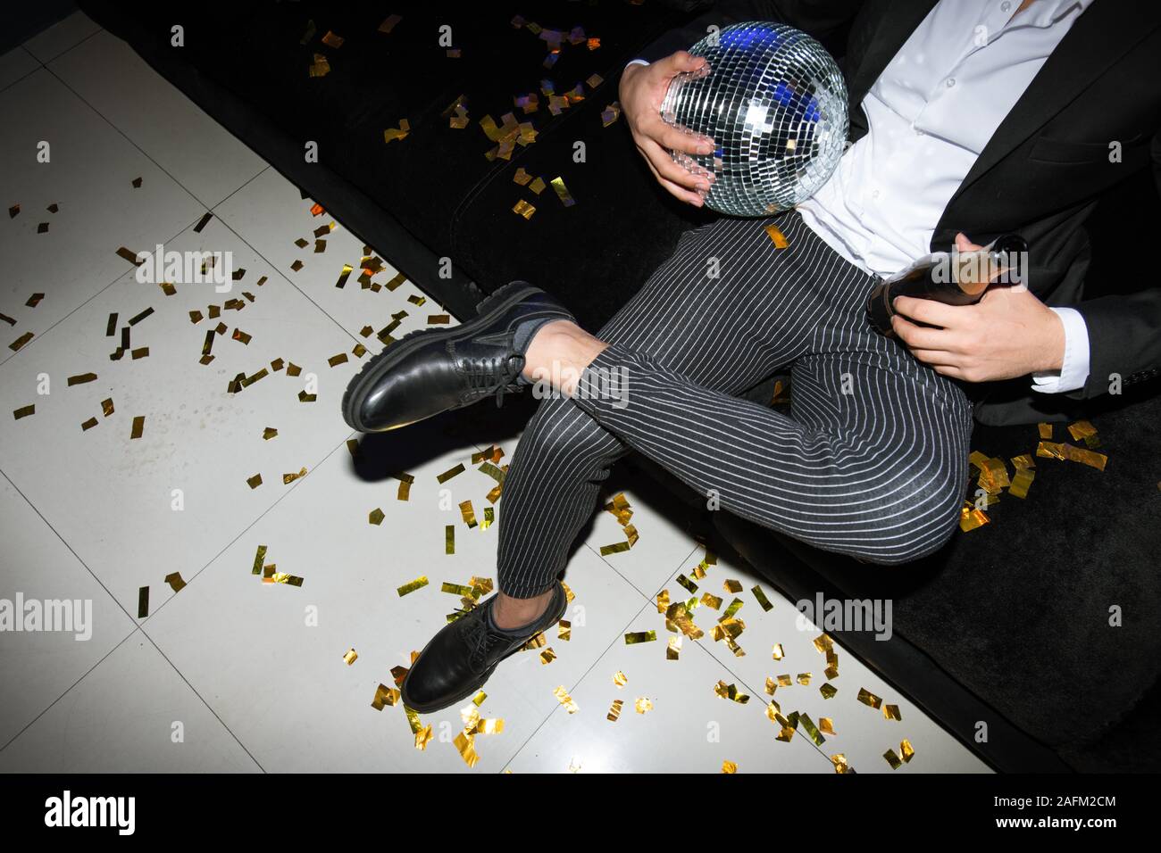 Les jambes de l'homme élégant avec boule disco et bouteille de champagne relaxing on couch Banque D'Images