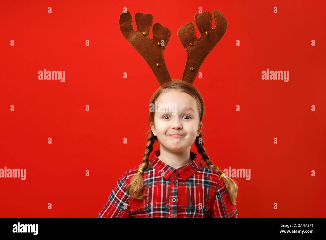 Heureux l'enfant drôle de Noël rouge dresse et deer cornes sur sa tête sur un fond de couleur. Petite fille émotionnelle de plaisir et de surprise. Banque D'Images