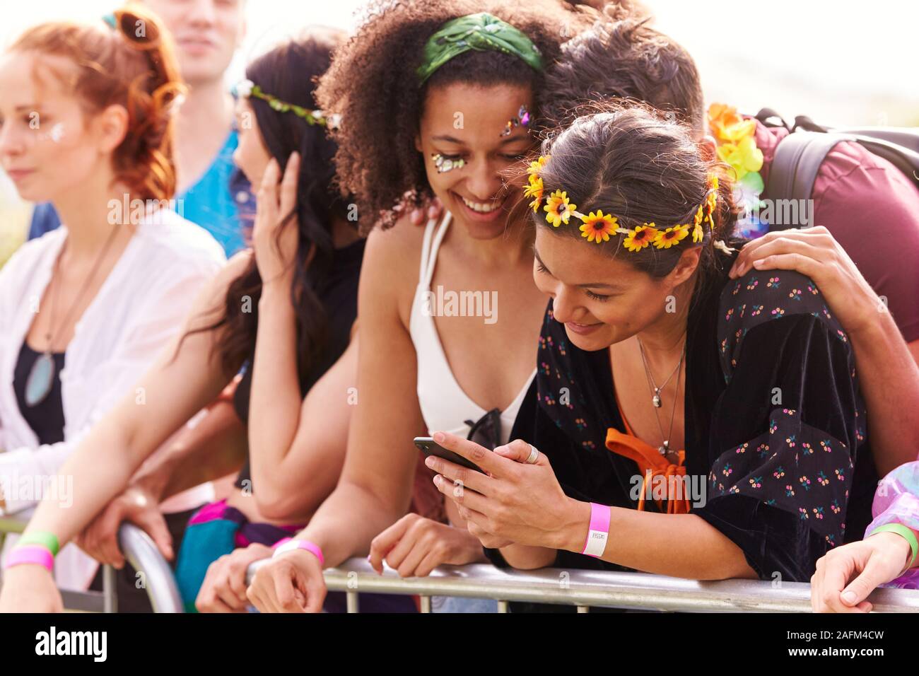 Jeunes amis en audience derrière barrière sur Festival de musique en plein air Looking At Mobile Phone Banque D'Images