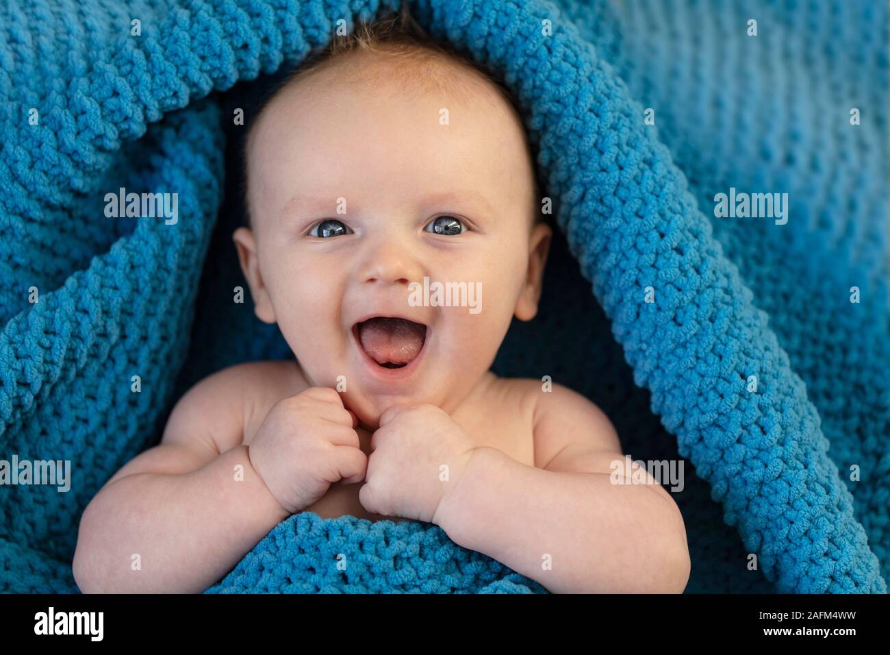 Une happy laughing baby enveloppé dans une couverture bllue Banque D'Images