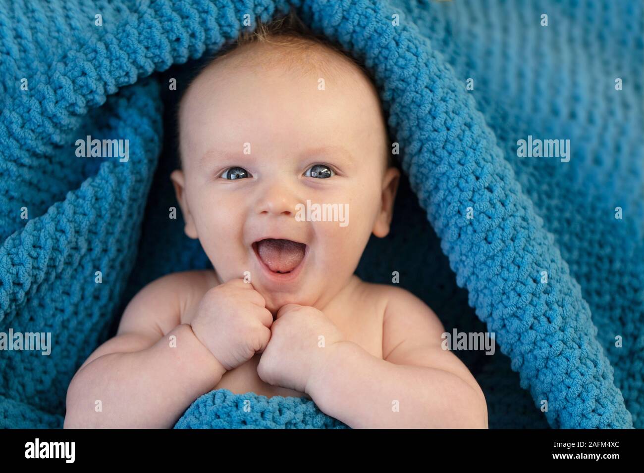 Une happy laughing baby enveloppé dans une couverture bllue Banque D'Images