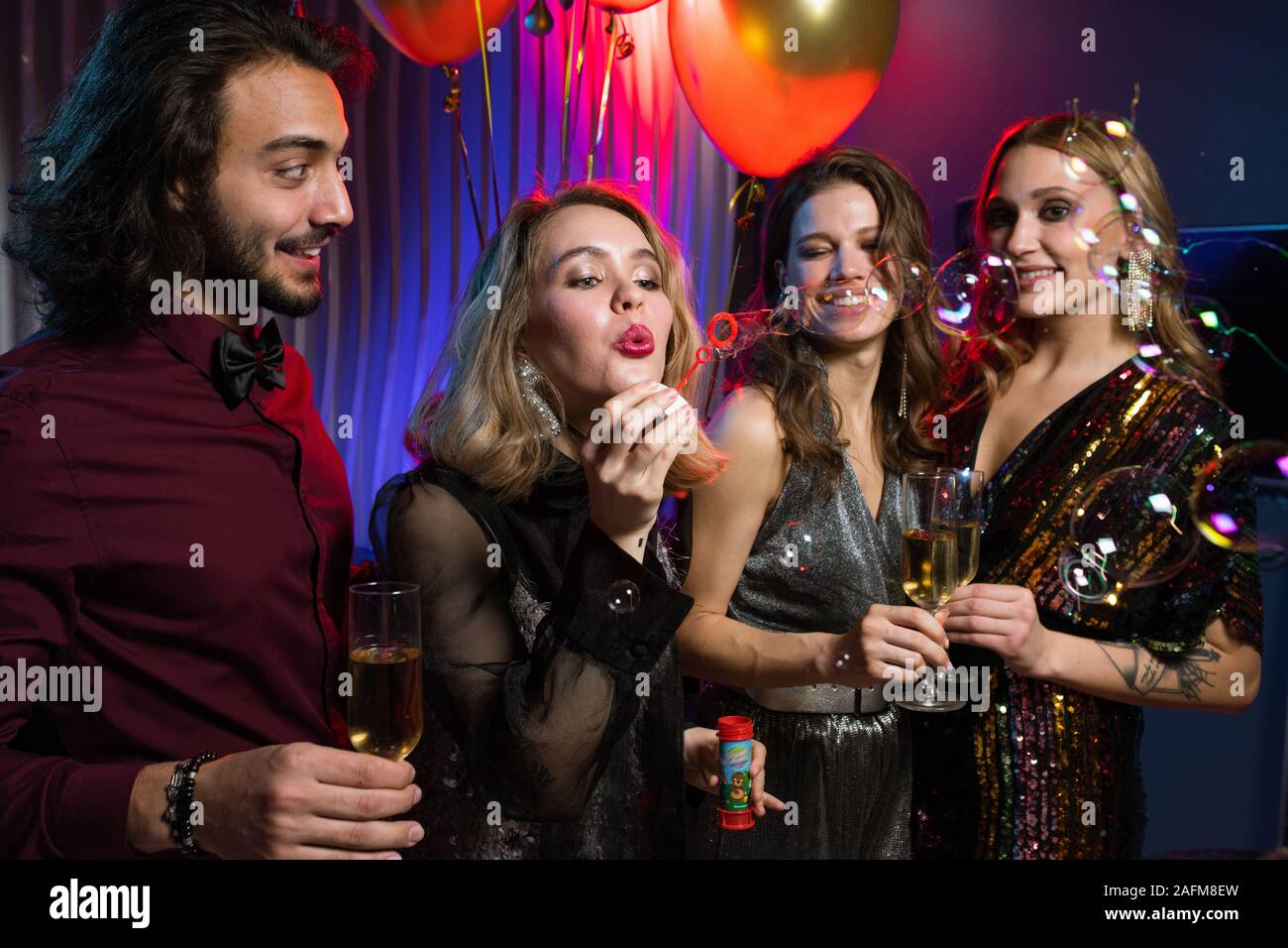 Jolie fille blonde soufflant des bulles de savon parmi ses amis dans le club de nuit Banque D'Images
