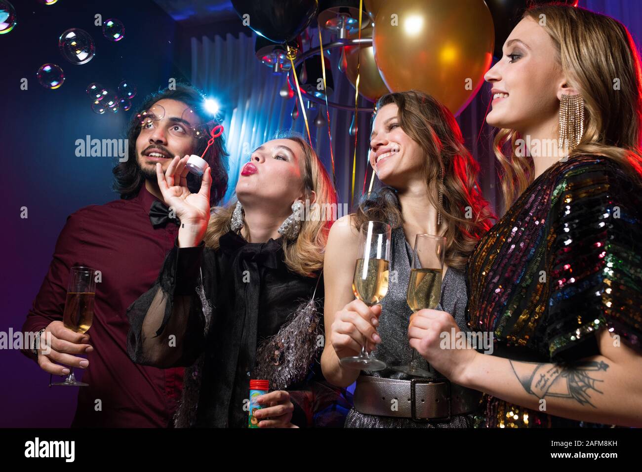 Glamorous girl blowing soap bubbles entre amis avec des flûtes de champagne Banque D'Images