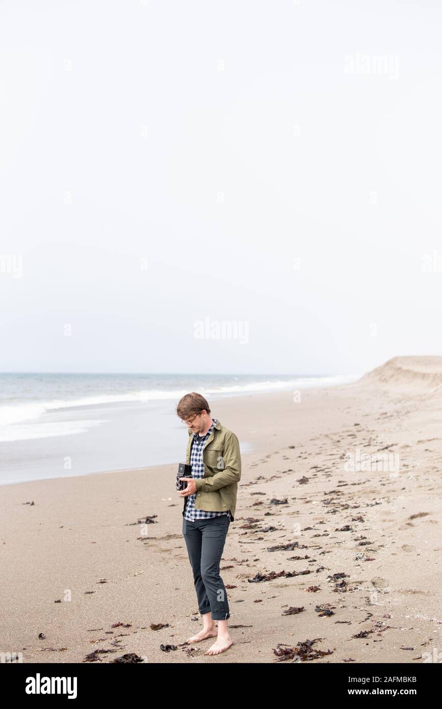 Jeune homme debout sur la plage tout en photographie avec appareil photo Banque D'Images