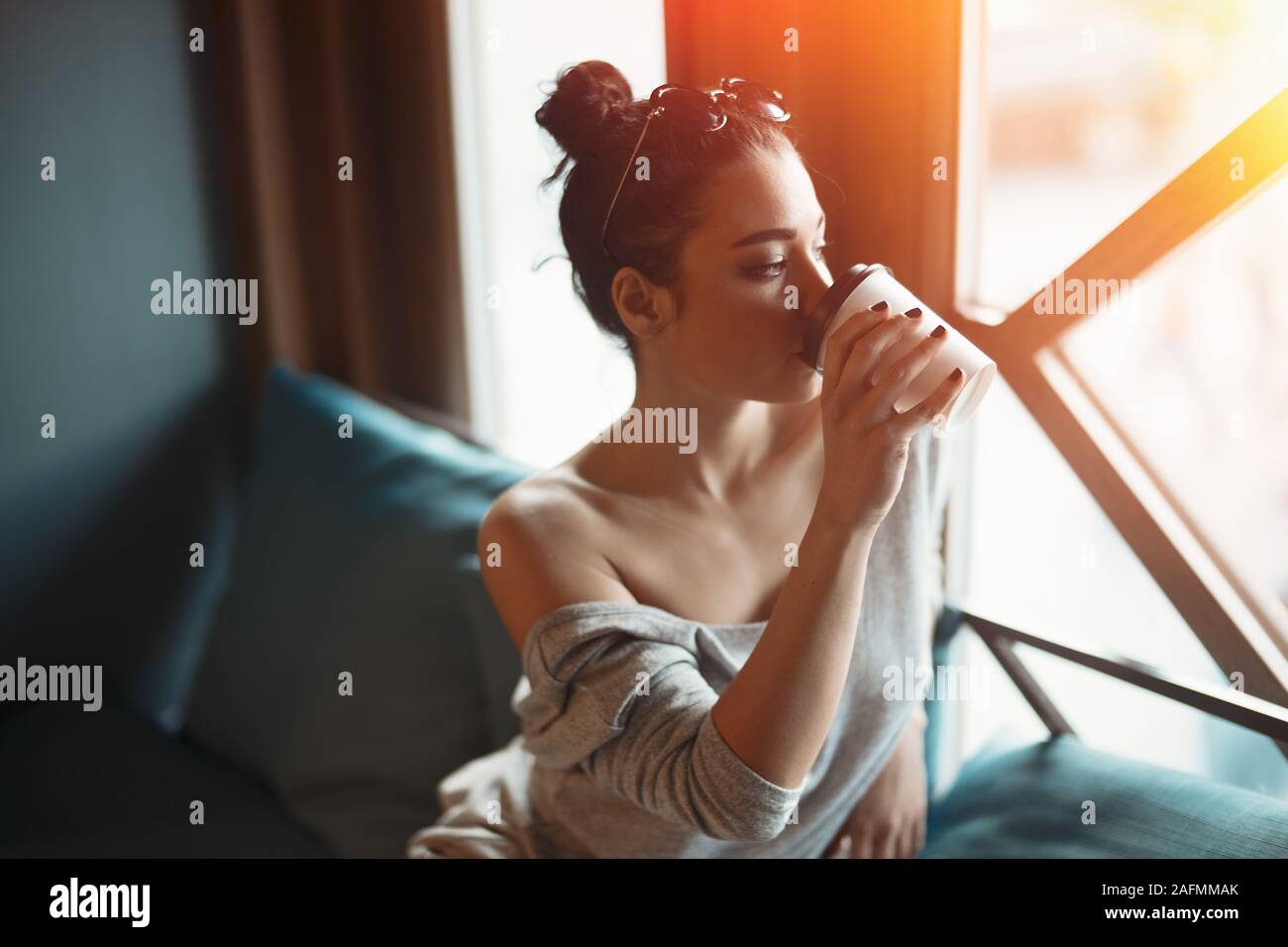 Jeune femme séduisante à par pensif Fenêtre, boire du café et essayer de dormir avant de travailler dans la journée, Sun Beam passe par la fenêtre et Illumi Banque D'Images