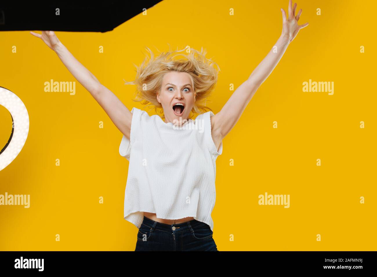 Grimaçant ludique blonde woman jumping avec les mains en l'air sur jaune Banque D'Images