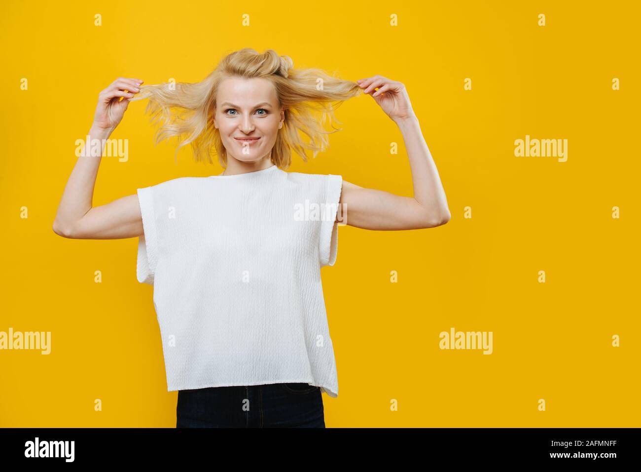 Femme blonde grimaçant ludique avec les mains sur sa taille sur jaune Banque D'Images