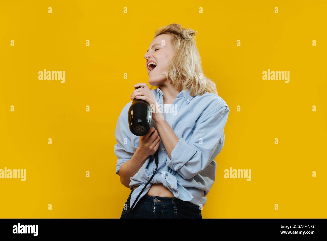 Blonde coiffure dame chanter dans un sèche-cheveux, l'utilisant comme microphone Banque D'Images