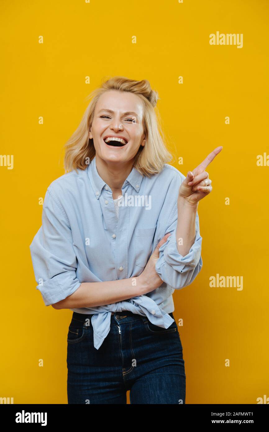 Femme blonde rire avec son index outstreched sur jaune Banque D'Images
