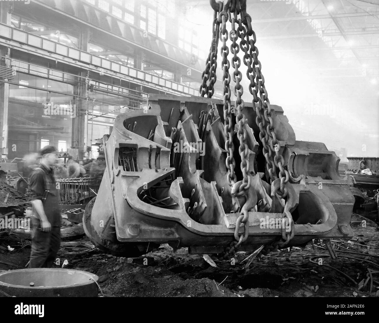 Un travailleur Allis Chalmers observe un heavy metal casting ascenseurs grues sur le sol de l'usine, ca. L'année 1930. Banque D'Images