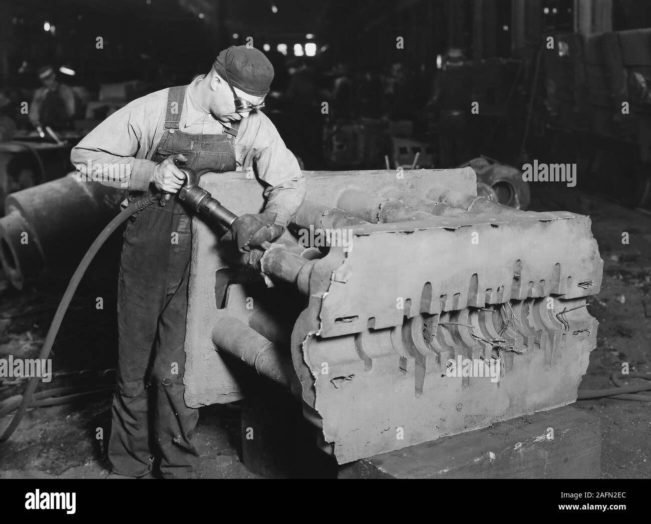 Un travailleur d'usine nettoie un casting sur un étage de la fonderie à Milwaukee, Wisconsin, ca. L'année 1930. Banque D'Images