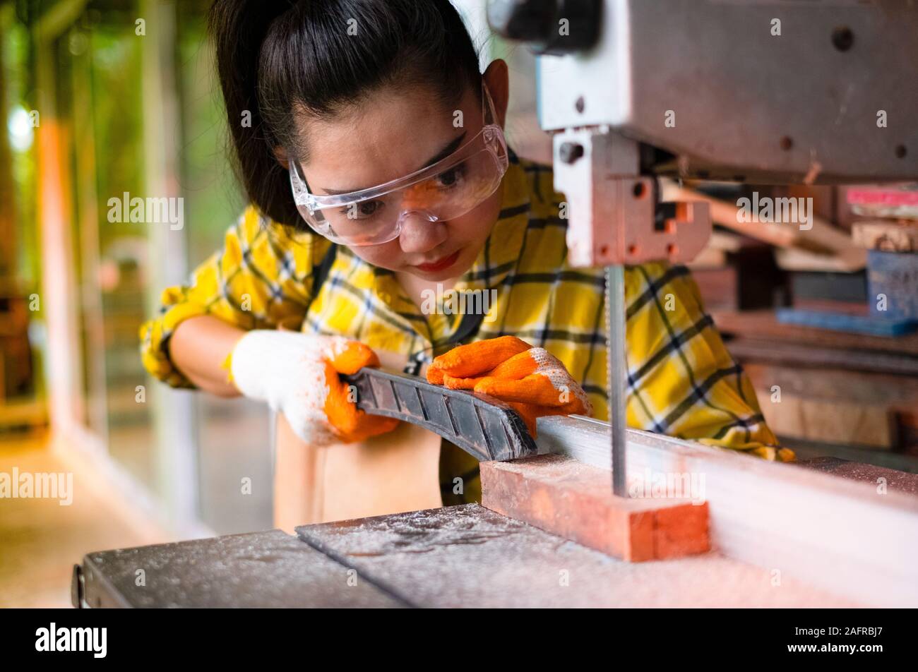 Comité permanent de l'artisanat des femmes est de couper du bois à un établi avec des outils électriques scies à ruban à carpenter machine dans l'atelier, le sciage des planches de travailleur wi Banque D'Images