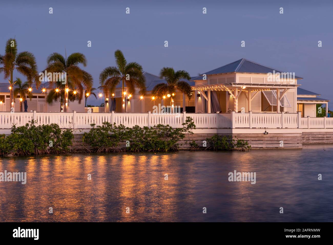 San Pedro, Ambergris Caye, Belize. Une vue d'un resort tropical avec des palmiers, ce qui reflète la lumière sur l'eau encore pendant l'heure bleue. Banque D'Images