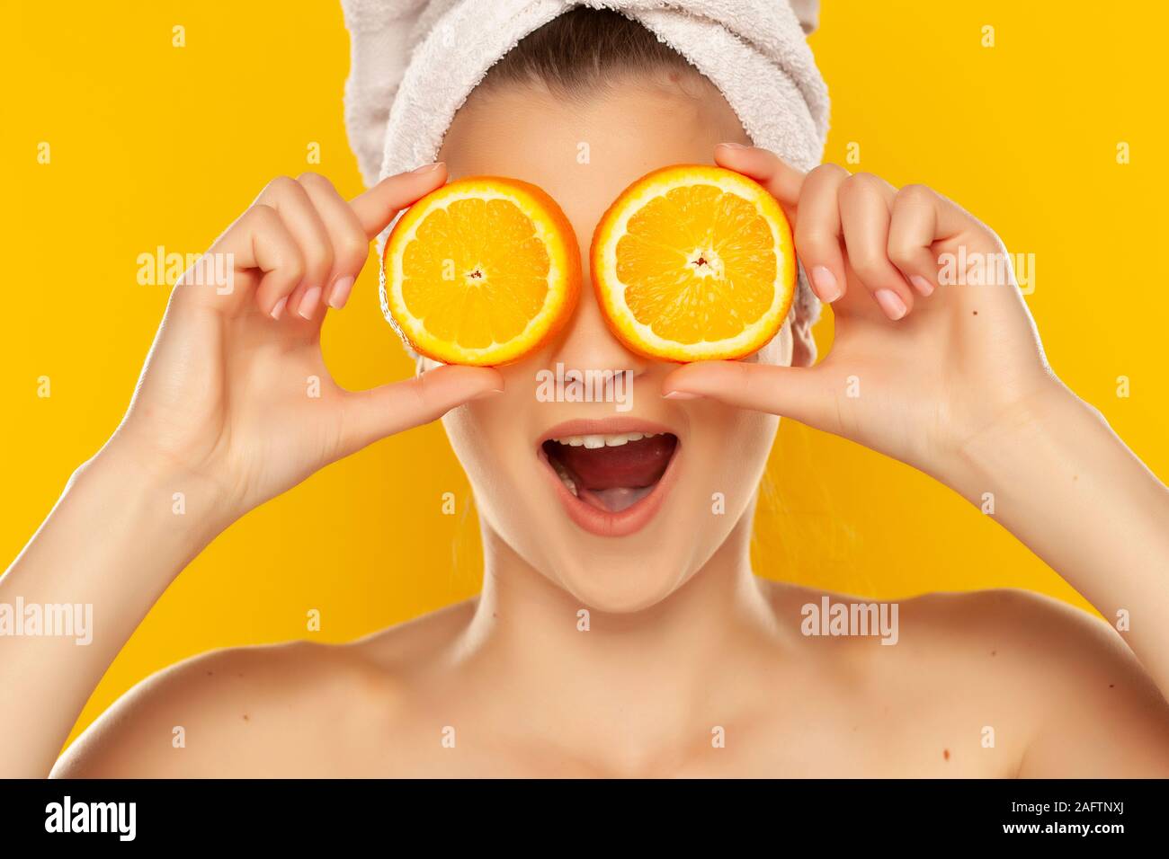 Belle jeune femme avec une serviette sur la tête d'oranges tranches tenant devant ses yeux sur fond jaune Banque D'Images