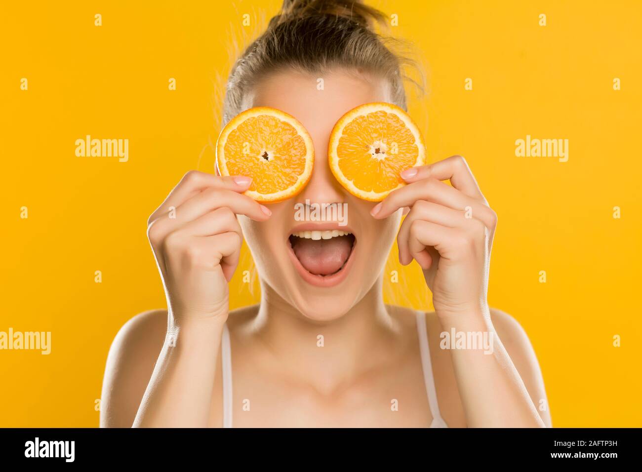 Young Beautiful woman holding tranches d'orange devant ses yeux sur fond jaune Banque D'Images