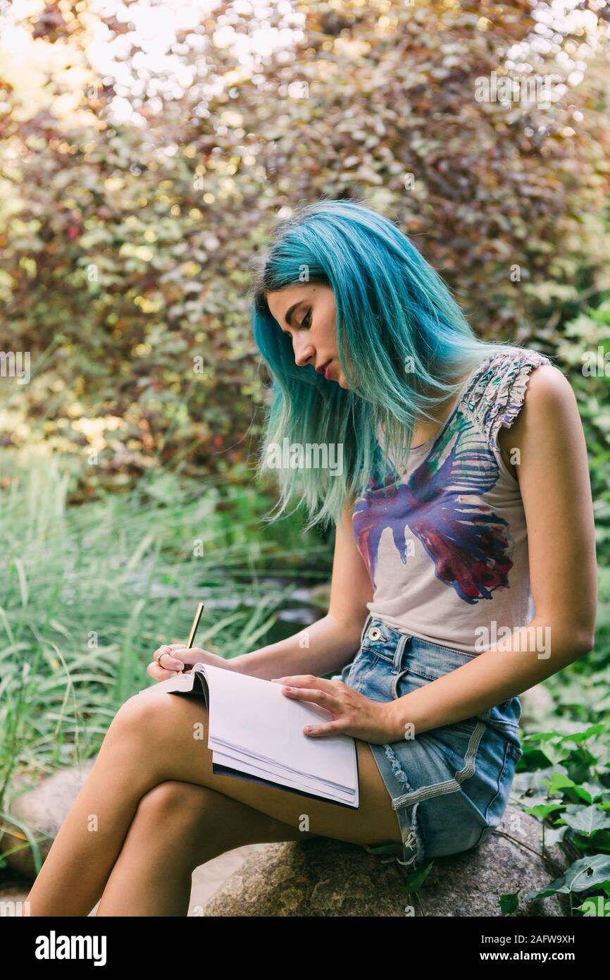 Jeune femme aux cheveux bleus écrit dans journal in park Banque D'Images