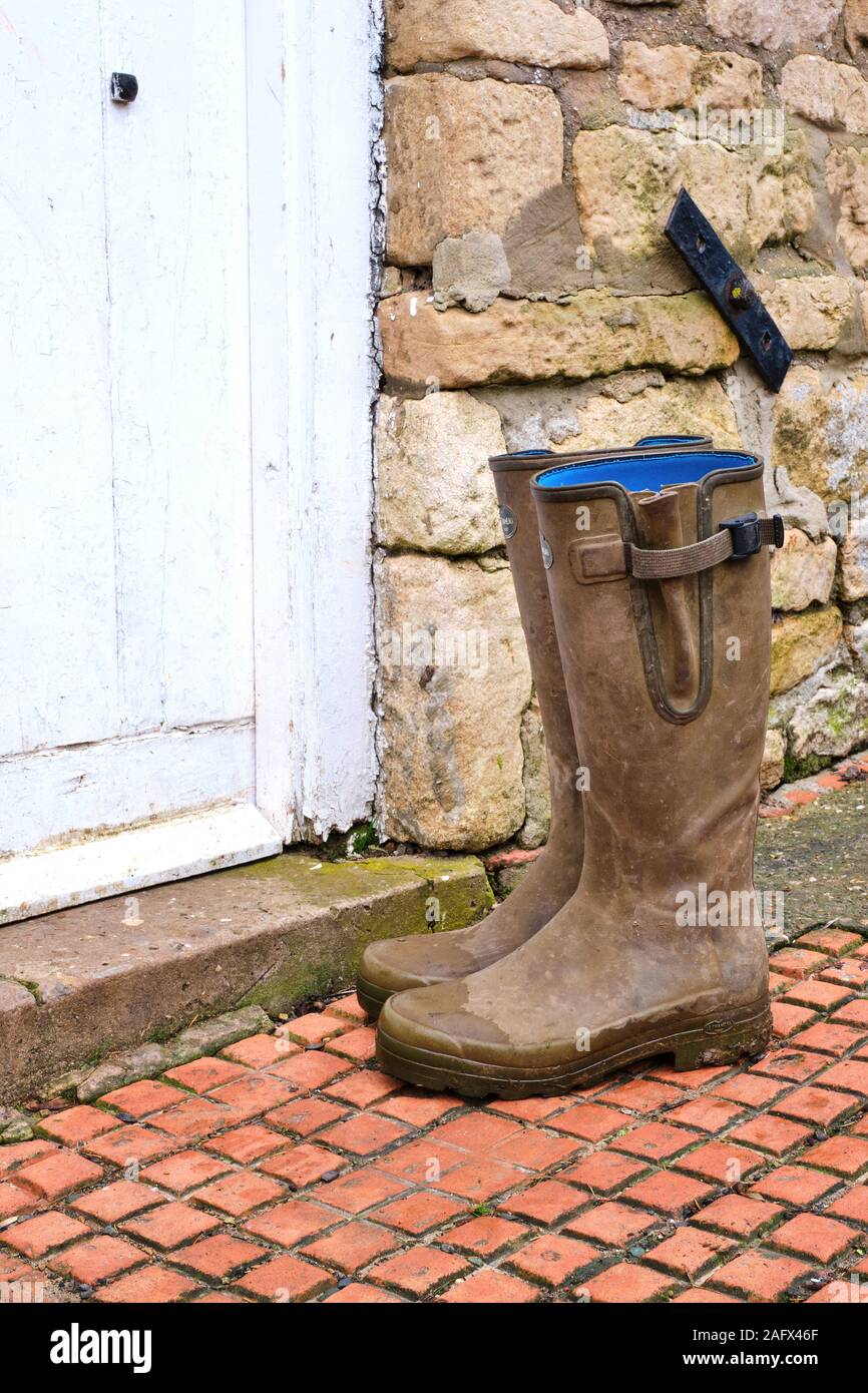 Vert bottes boueuses à l'extérieur de la porte d'une porte blanche à une maison de ferme en pierre. Couvre-bottes en caoutchouc bottes de gomme blucher boot Banque D'Images