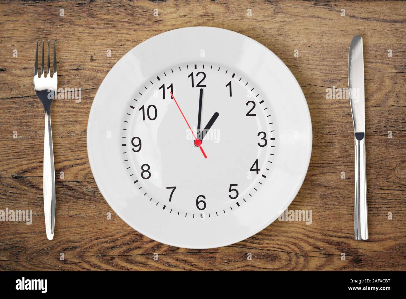 Couteau, fourchette, assiette blanche avec horloge montrant l'heure du déjeuner sur la vieille table en bois Banque D'Images