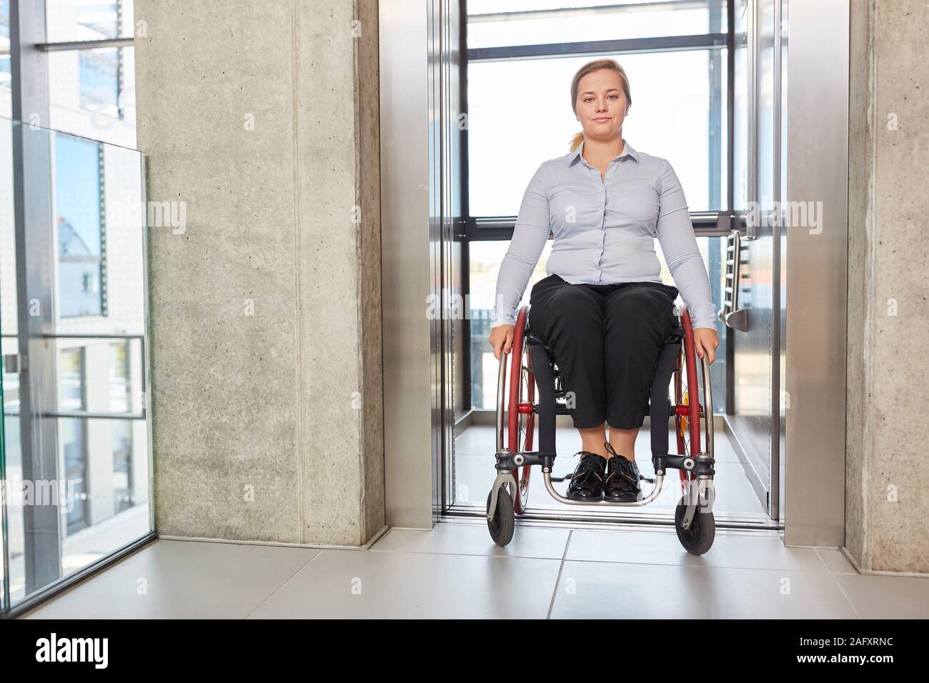 En tant que femme d'un utilisateur de fauteuil roulant dans l'ascenseur de l'entreprise sans obstacle sur la voie Banque D'Images