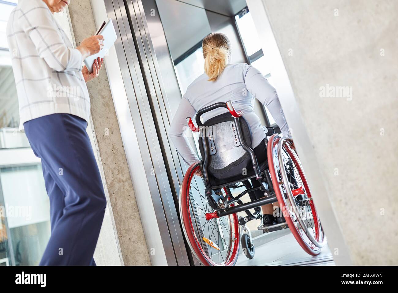 Femme dans un fauteuil roulant qui voyage avec l'ascenseur de l'entreprise La société Banque D'Images
