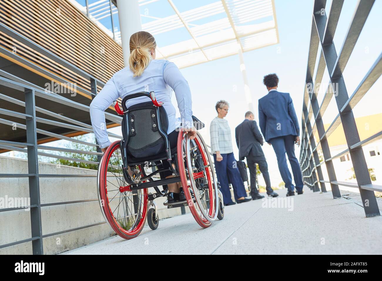 En tant que femme handicapée en fauteuil roulant sur une rampe avec d'autres travailleurs Banque D'Images