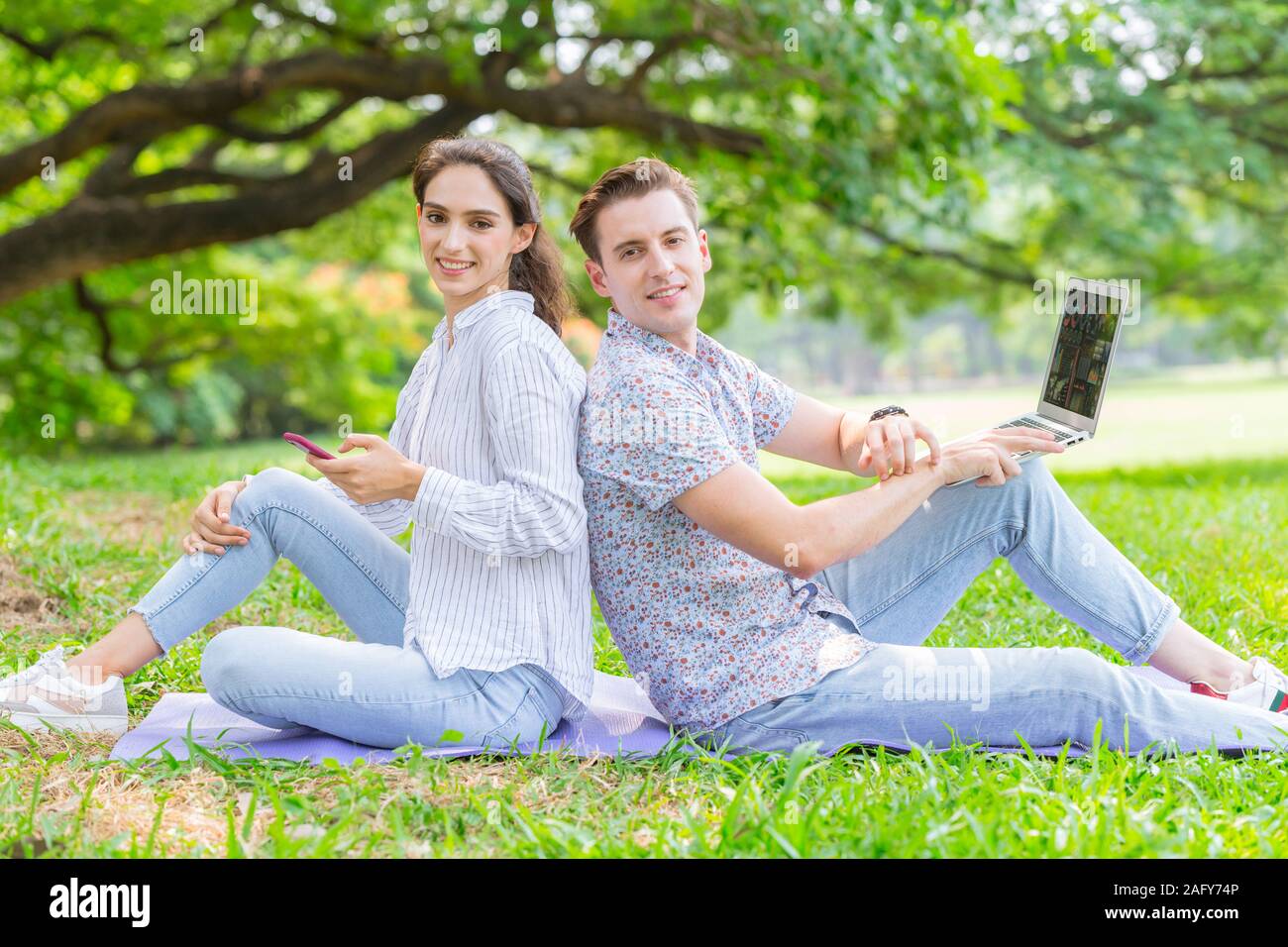 Couple d'amoureux avec appareil de technologie de vie, à l'aide de smartphone et ordinateur portable avec green nature piscine arrière-plan. Banque D'Images