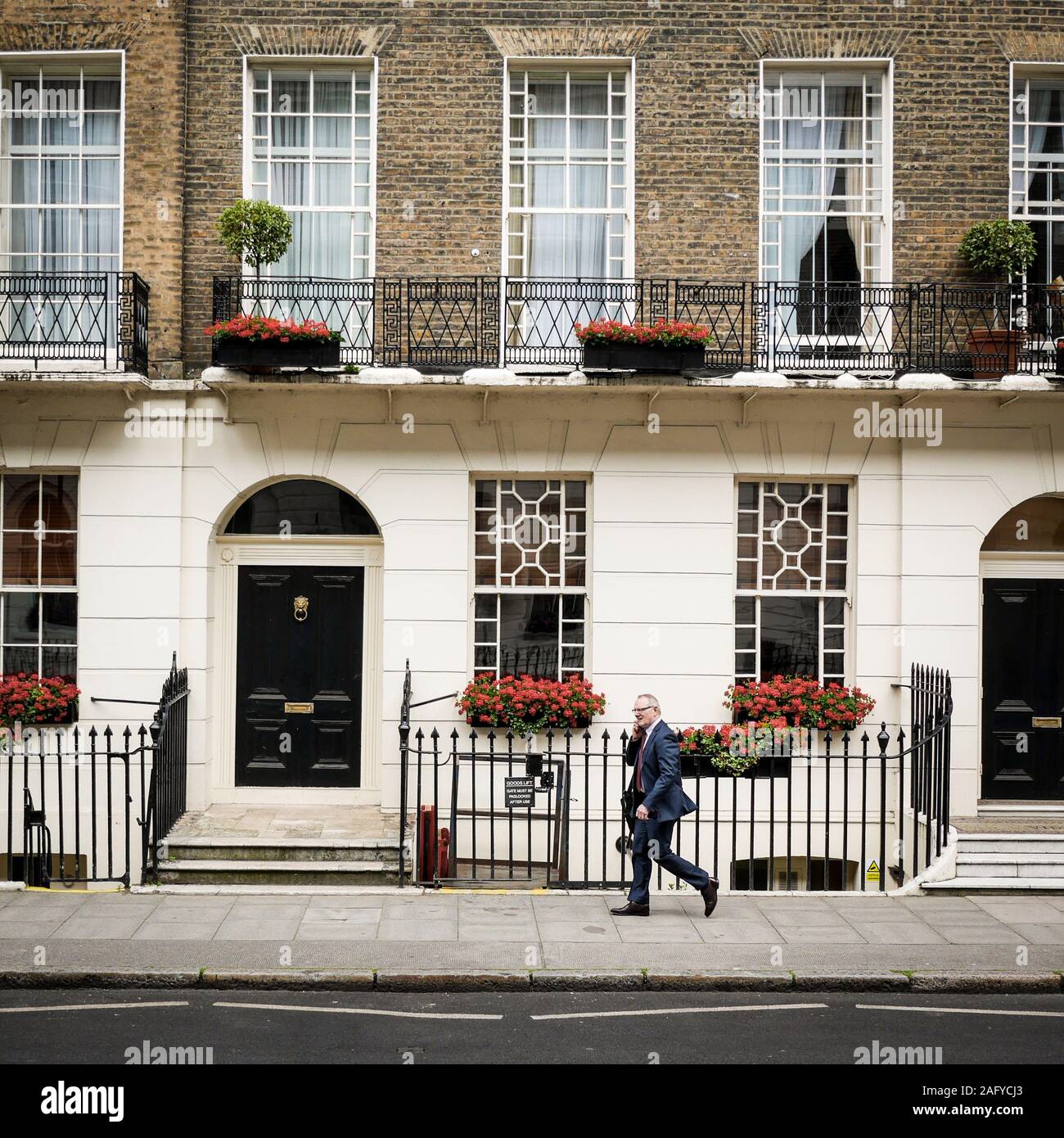 Un Londres traditionnelle maison de ville géorgienne à Bloomsbury, avec un homme d'affaires habillés en passant par la conversation sur son portable Banque D'Images