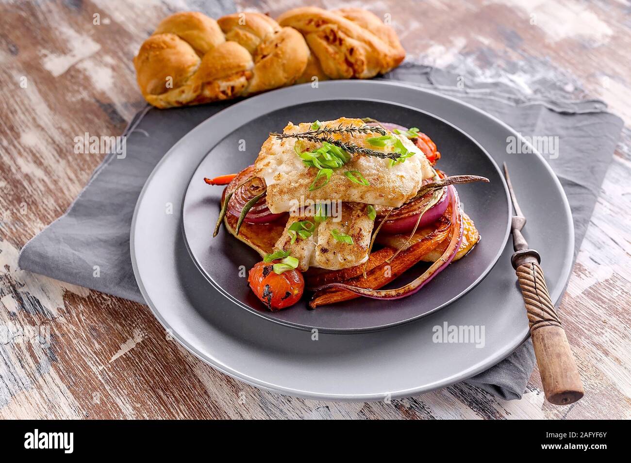 Filet de morue appétissante avec oignon rouge et d'herbes, pommes de terre au four et des carottes sur un plat dans une plaque gris sur une serviette. Fruits de mer sains et savoureux Banque D'Images