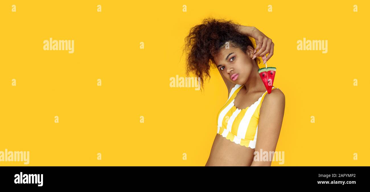 Fashion african girl holding candy regarde appareil isolé sur fond jaune Banque D'Images